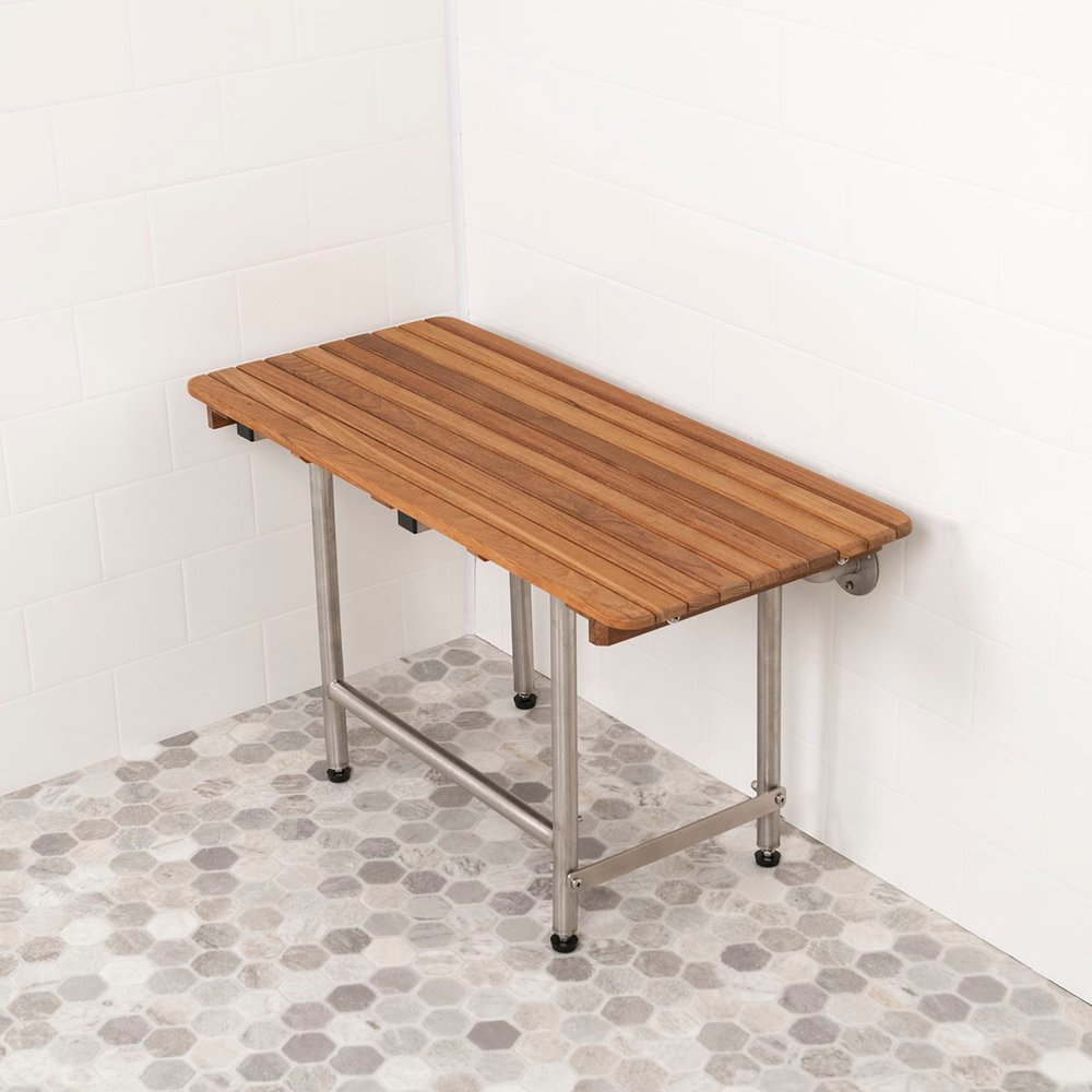 Brown teak rectangular shower bench with stainless steel legs on a hexagonal tile floor and white subway tile wall.