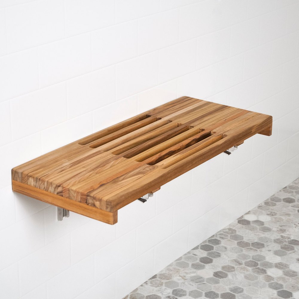 Wall-mounted teak shower bench with slatted top in a bathroom with white subway tile and hexagonal floor tiles.