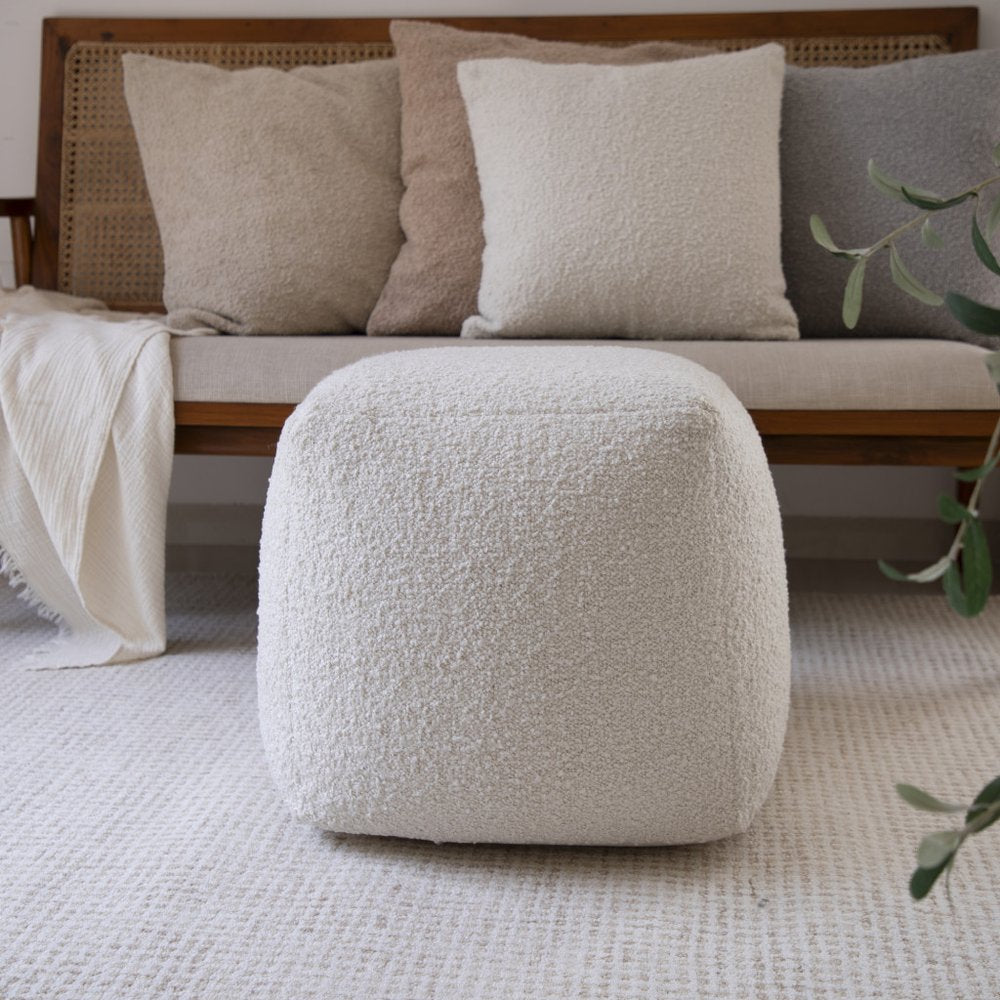 18" Beige Polyester Cube Outdoor Pouf Ottoman styled in a furnished interior with a dark brown wall on a tiled floor.