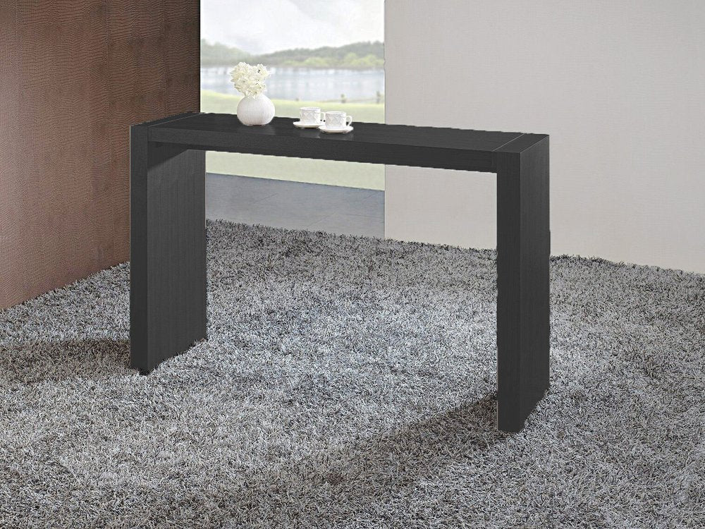 Espresso wood bar height bar table with two cups and a vase on top, set on a grey shag rug in front of a window.