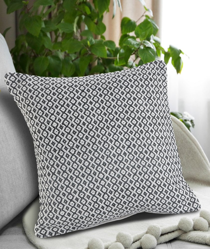 A black and white diamond pattern throw pillow rests on a gray couch with a green plant in the background.