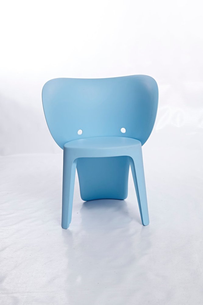 A light blue plastic juvenile chair with two holes in the backrest sits on a white surface.