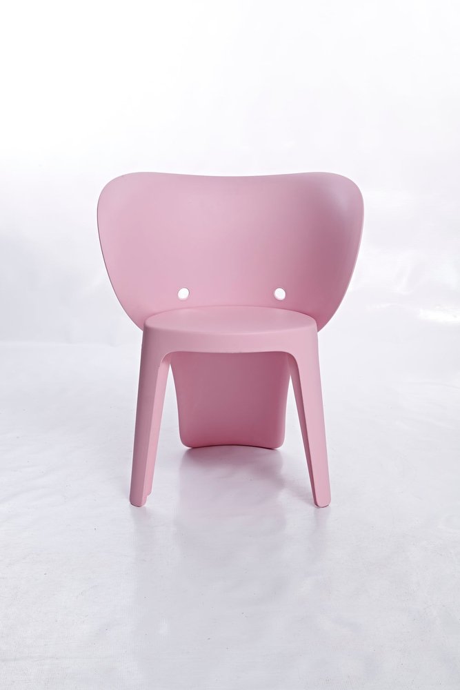 A pink heavy-duty plastic juvenile chair with a curved back and two circular holes, set against a white background.