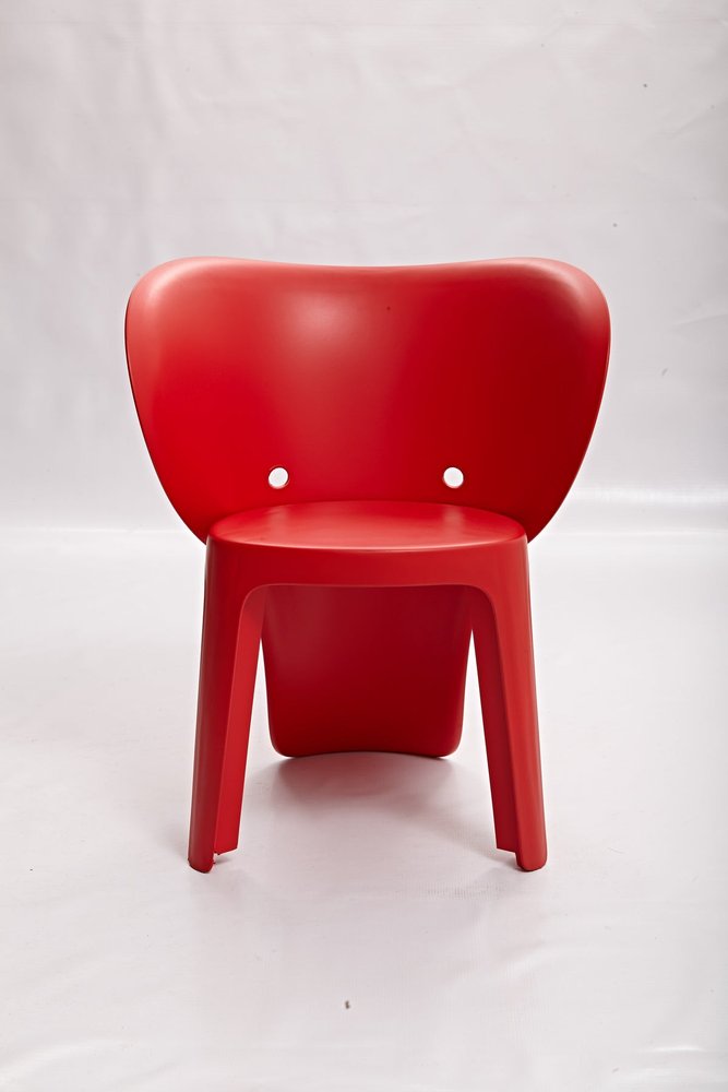 Red heavy duty plastic juvenile chair with a curved back and two circular holes, on a white background.