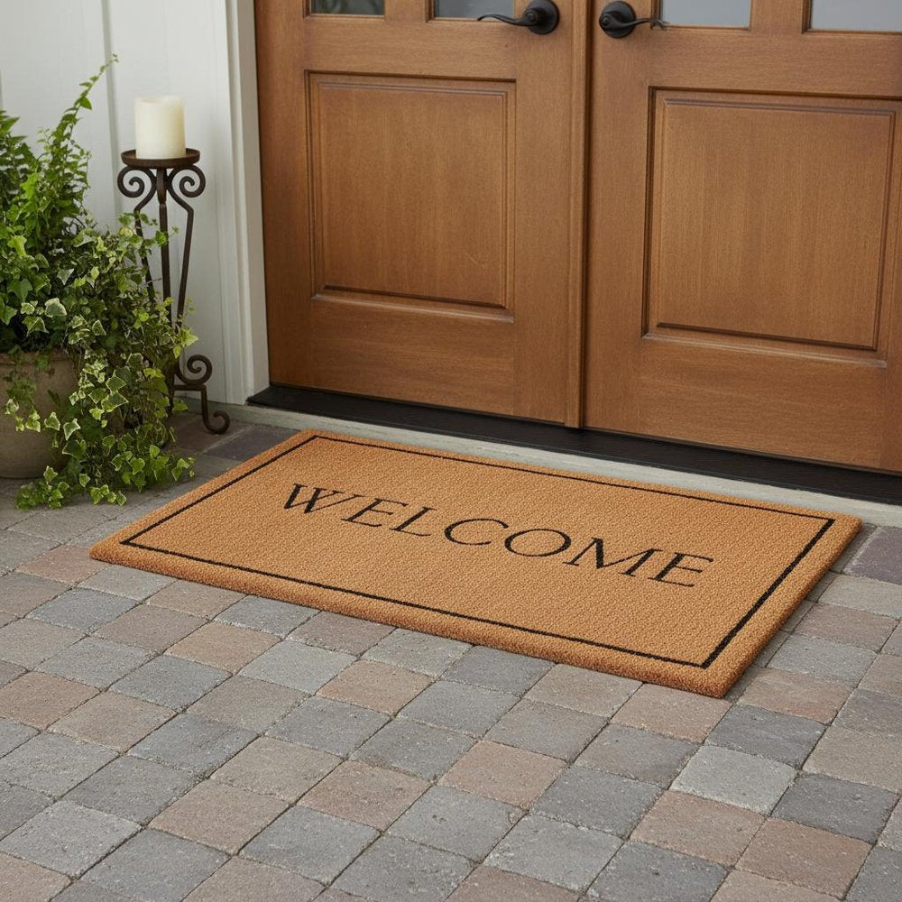 30" X 48" Natural and Black Coir Welcome Outdoor Door Mat styled in a furnished interior with a mahogany wall on a tiled floor in tan.
