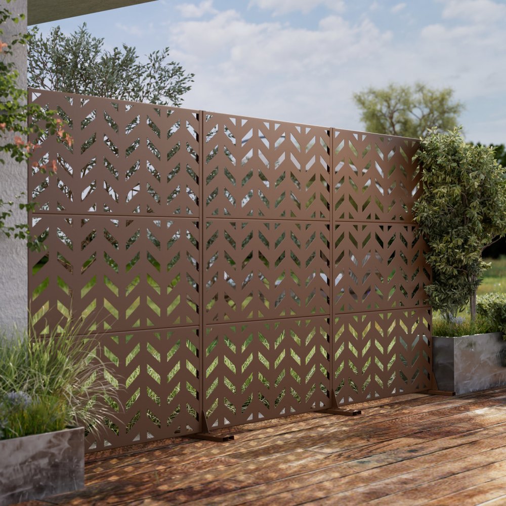 Brown steel three-panel outdoor privacy screen with chevron pattern on a wooden deck with plants and sky background.