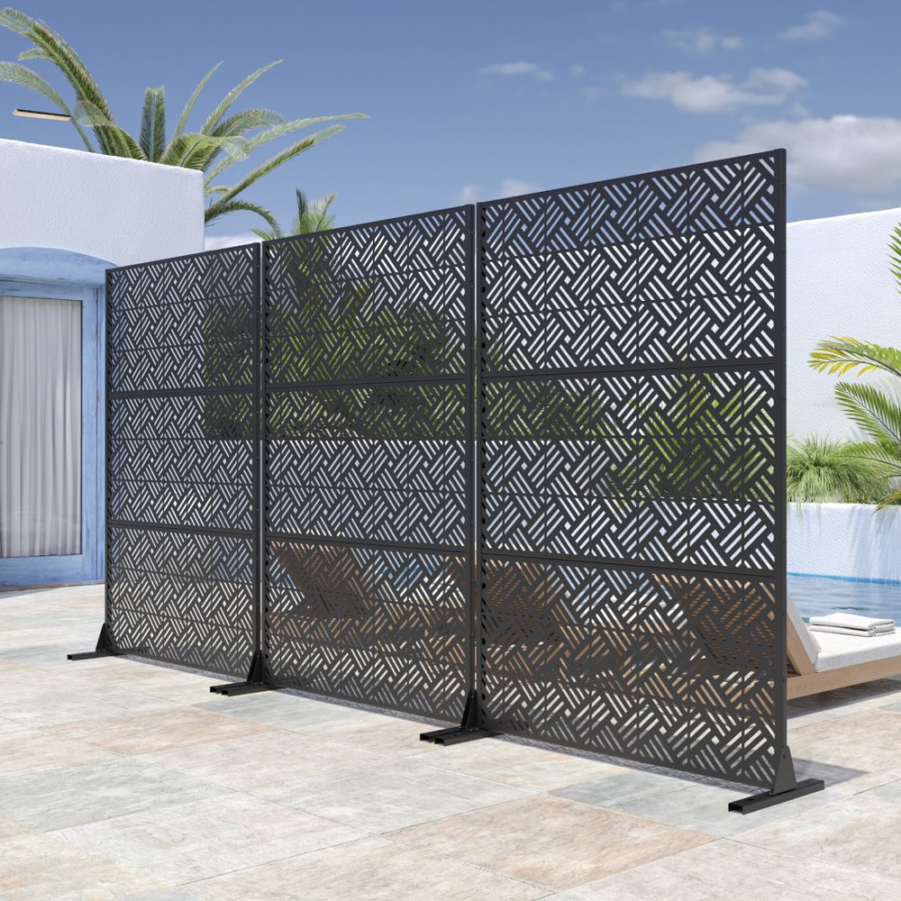 Black steel three-panel outdoor privacy screen with geometric pattern on a patio with a pool and lounge chair.