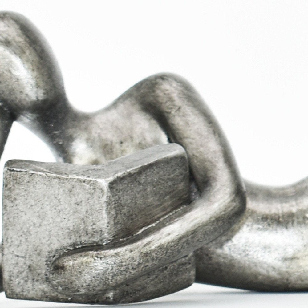 A close-up of a pewter-colored resin sculpture of two people holding a block on a white background.