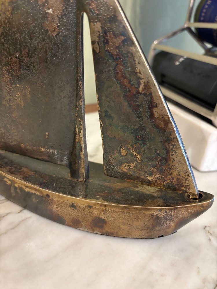 12" Rust Aluminum Decorative Sailboat Tabletop Sculpture styled in a furnished interior with a dark brown wall on a tiled floor in dark brown metal.