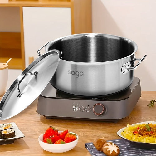 A silver stainless steel stock pot with lid sits on a gray induction cooktop on a wooden table, with food in bowls in the foreground.