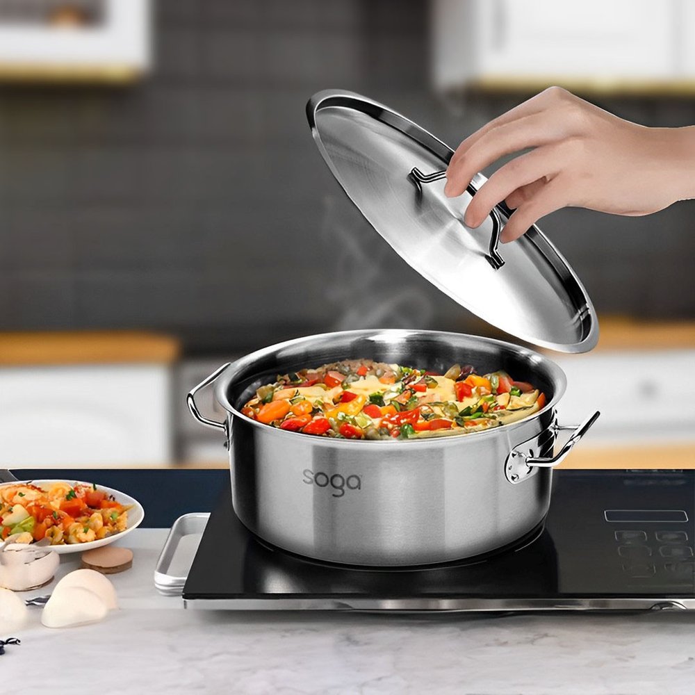 16" Silver Stainless Steel Stock Pot - 10.24" H x 15.75" W x 10.24" D styled in a furnished interior with a dark wall on a off-white floor.