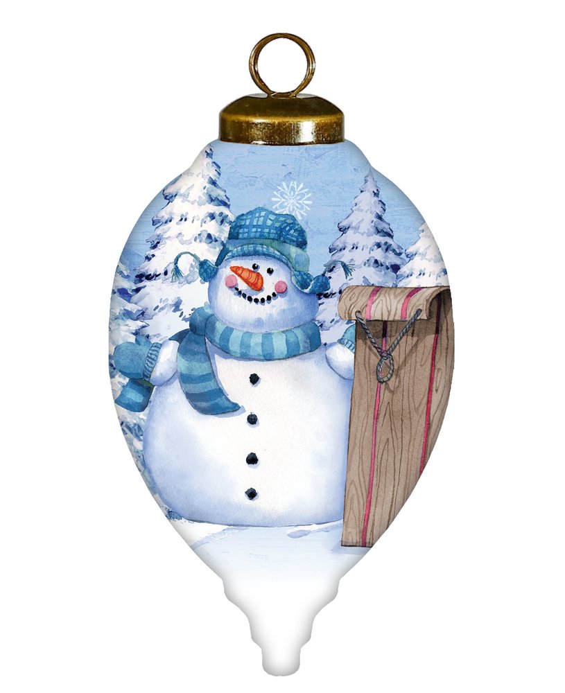 Glass finial ornament with a hand-painted snowman in a blue hat and scarf, holding a wooden sled, against a snowy forest background.