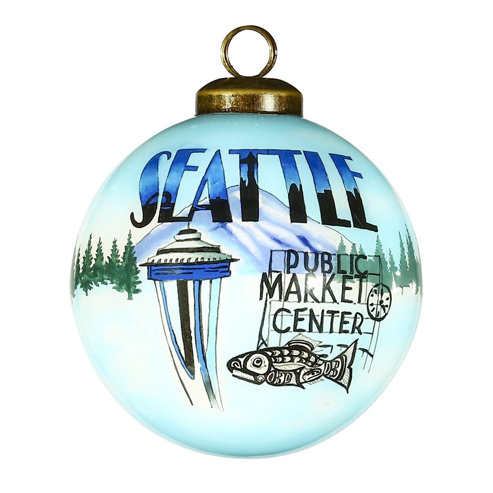 A light blue glass ball ornament with a hand-painted Seattle scene featuring the Space Needle, Public Market Center sign, and a fish.