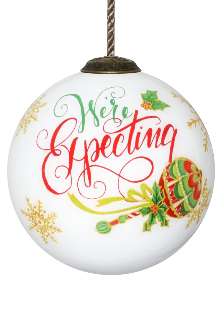 White glass Christmas ornament with "We're Expecting" in red and green script, gold snowflakes, and festive holiday accents.