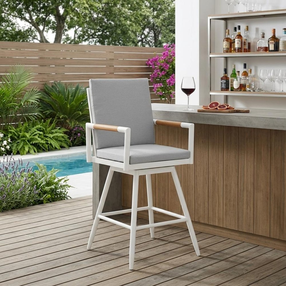 48" Light Gray Metal Swivel Outdoor Bar Height chair with Footrest shown outdoors on a patio with greenery.