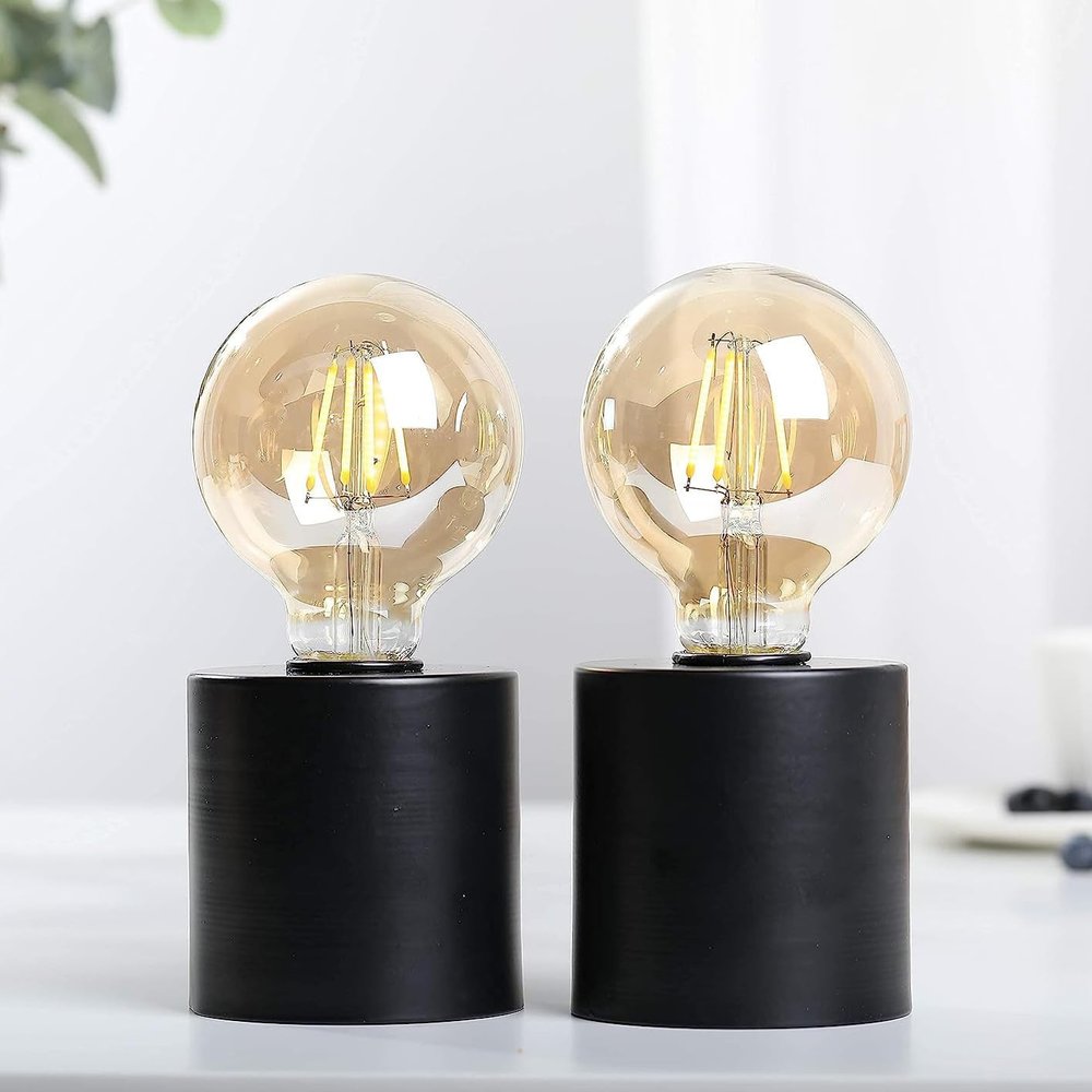 Two black cylinder lamp bases with amber Edison bulbs and cone shades on a white surface.