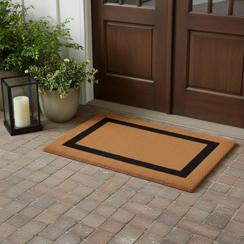 36" X 60" Brown and Black Coir Outdoor Door Mat styled in a furnished interior with a dark brown wall on a wood floor.