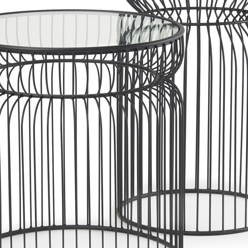 Close-up of two black metal wire round drum end tables with clear glass tops on a white background.