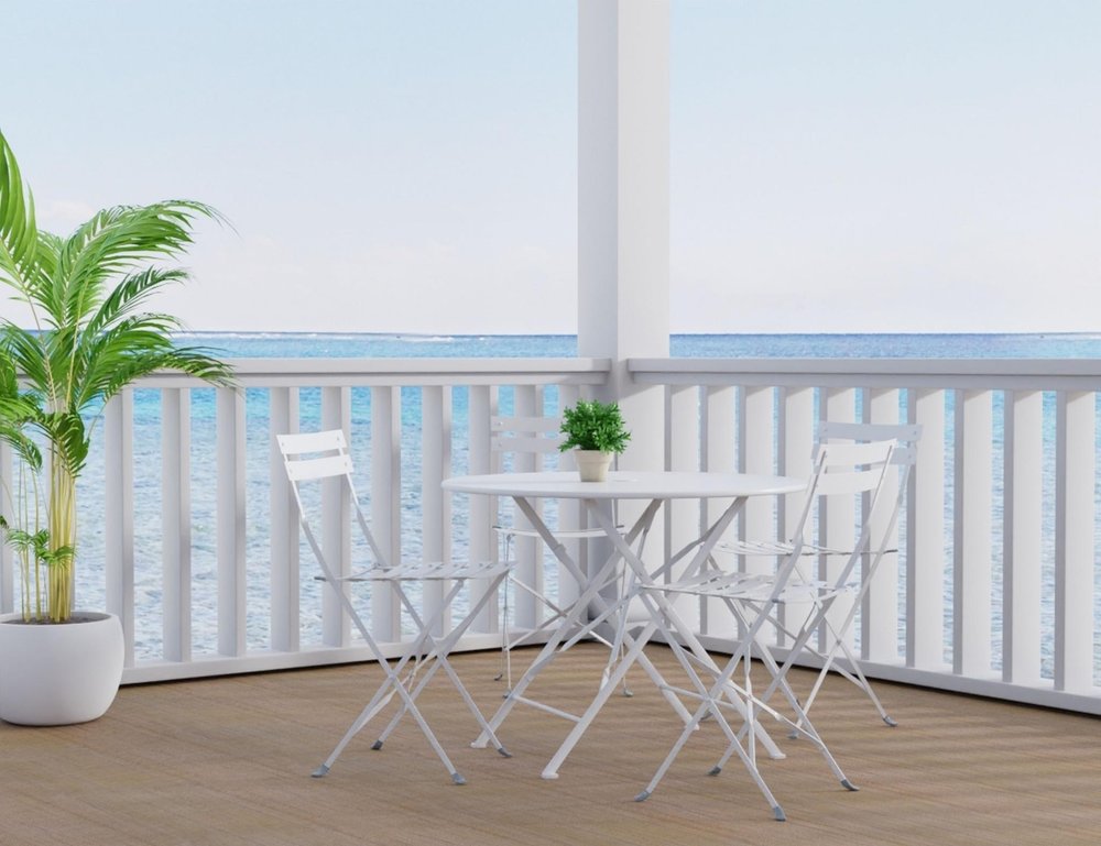 36" White Rounded Aluminum Folding Outdoor Dining Table with Umbrella Hole shown outdoors on a patio with greenery.