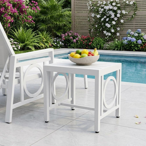 White metal outdoor side table with circular cutouts next to a pool with fruit in a bowl on top.
