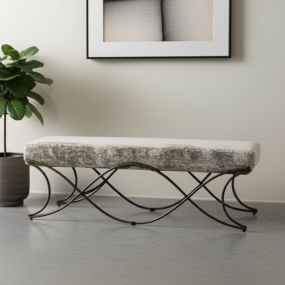 55" Gray and Gold Chenille and Metal Upholstered Bench styled in a furnished interior with a light gray wall on a tiled floor.