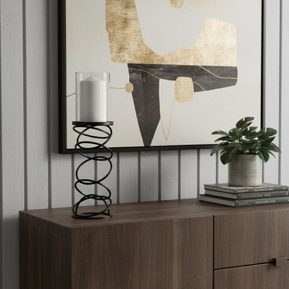 17" Black Geometric Glass And Metal Tabletop Pillar Candle Holder displayed on a dark wood tabletop in a furnished interior against an off-white wall.