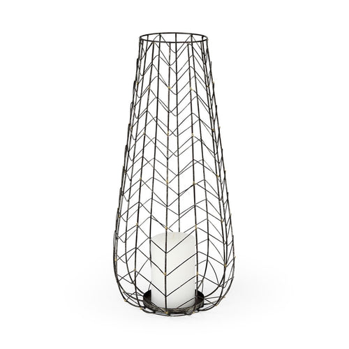 Tall, black distressed metal lattice hurricane candle holder with a white candle inside on a white background.