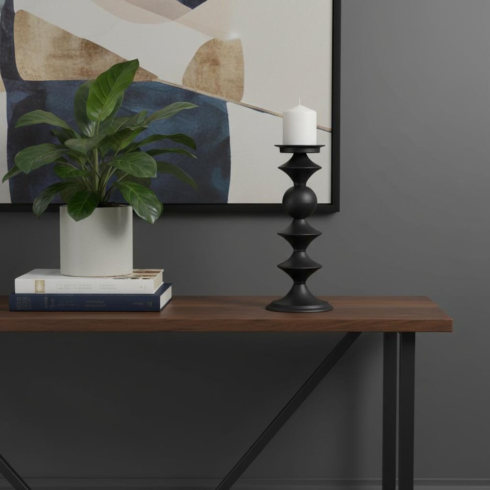 13" Black Metal Tabletop Pillar Candle Holder. Matte black metal pillar candle holder with a white candle, placed on a dark wood console against a gray wall.