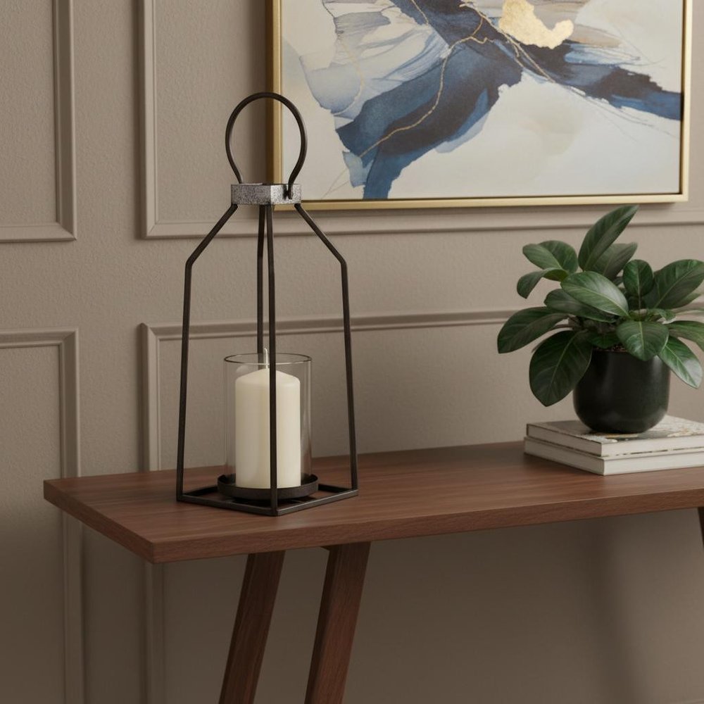 16" Black Distressed Geometric Metal And Glass Tabletop Votive Candle Holder displayed on a dark wood tabletop in a furnished interior against a tan wall.