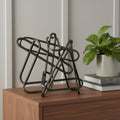 12" Black Metal Abstract Tabletop Sculpture styled in a furnished interior with a light gray wall on a dark wood floor.