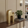 11" Antiqued Brass Aluminum Modern Abstract Tabletop Sculpture styled in a furnished interior with a tan wall on a dark wood floor.