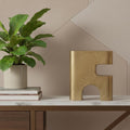 10" Brass Aluminum Tabletop Sculpture styled in a furnished interior with a tan wall on a dark wood floor.