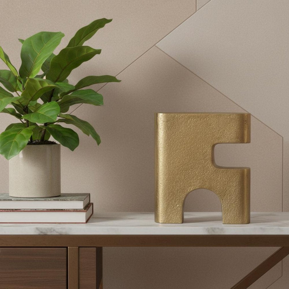 10" Brass Aluminum Tabletop Sculpture styled in a furnished interior with a tan wall on a dark wood floor.