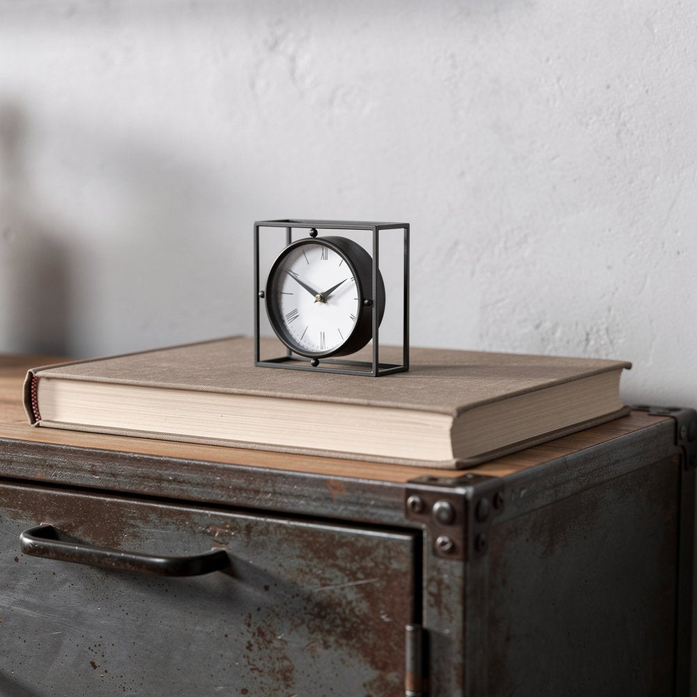 3" Black Distressed Metal Table Clock displayed on a tabletop in a furnished interior against an off-white wall.