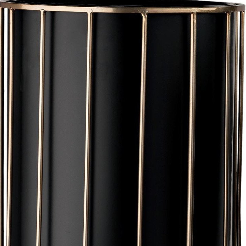 Close-up of a black cylindrical planter with gold metal cage accents.