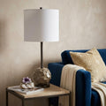 25" Gray Round Bedside Lamp With Drum Shade styled in a furnished interior with a tan wall on a dark wood floor.