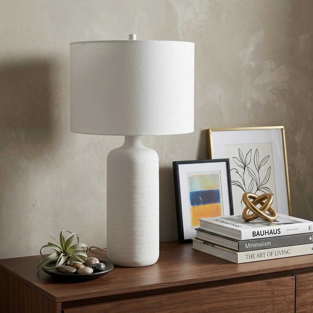 31" White Round Bedside Lamp With Drum Shade styled in a furnished interior with a tan wall on a dark wood floor.