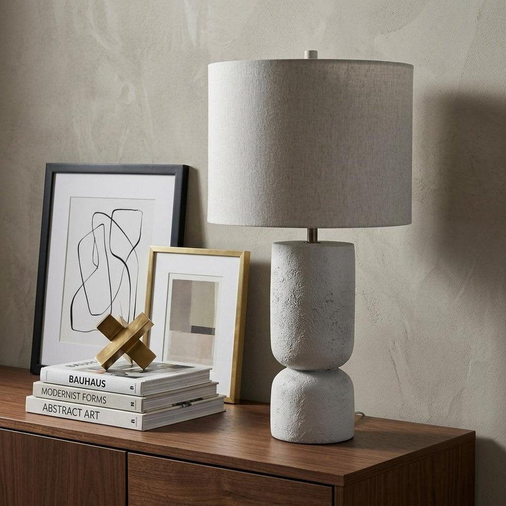 28" White Round Bedside Lamp With Drum Shade styled in a furnished interior with a light gray wall on a dark wood floor.