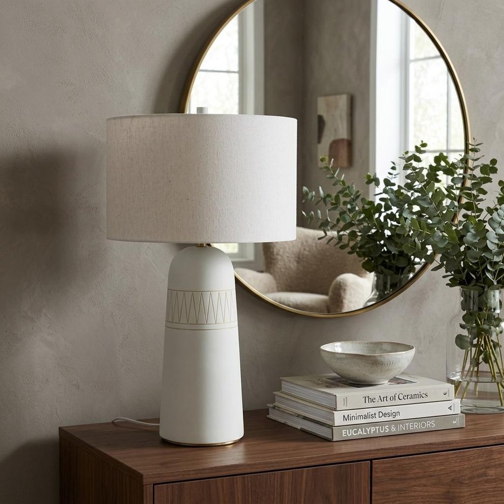 30" Cream Round Bedside Lamp With Drum Shade styled in a furnished interior with a tan wall on a dark wood floor.