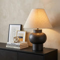 26" Black Round Bedside Lamp With Empire Shade styled in a furnished interior with a cream wall on a black floor.