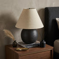 24" Black Round Bedside Lamp With Empire Shade styled in a furnished interior with a tan wall on a dark wood floor.