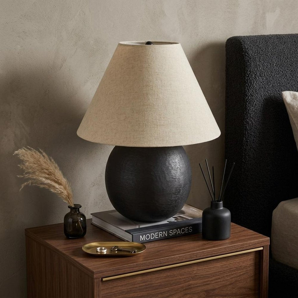 24" Black Round Bedside Lamp With Empire Shade styled in a furnished interior with a tan wall on a dark wood floor.