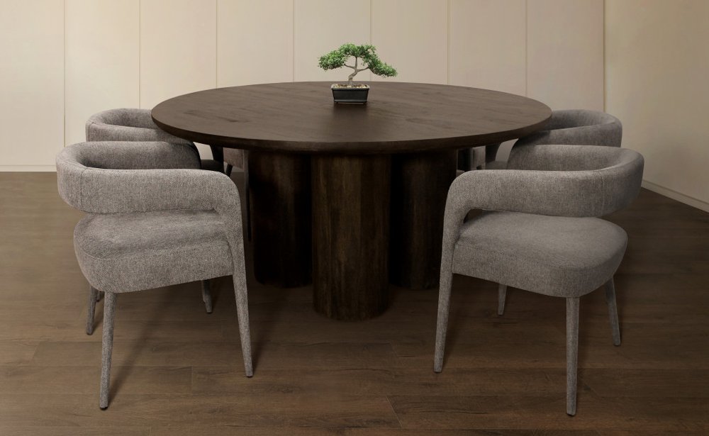 Dark brown solid wood round dining table with six grey upholstered chairs in a room with light walls and wood floor.