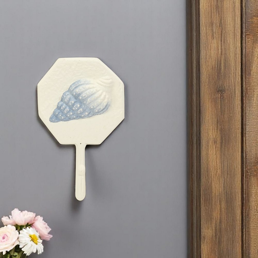 4" Blue And Cream Cast Iron Conch Shell Wall Hook styled in a furnished interior with a light gray wall on a tiled floor.