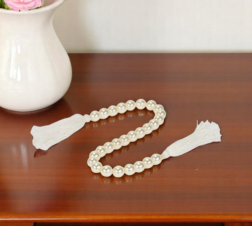 White pearl bead garland with white tassels draped on a wooden surface next to a white vase.