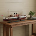 11" Unfinished Wood Hand Painted Model Boat styled in a furnished interior with a tan wall on a dark wood floor in tan wood.