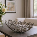 20" Silver Aluminum Abstract Circles Oval Decorative Bowl styled in a furnished interior with a light gray wall on a charcoal floor.