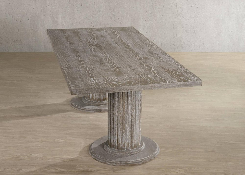 Rectangular gray wood dining table with a distressed finish and double fluted pedestal bases on a light wood floor.