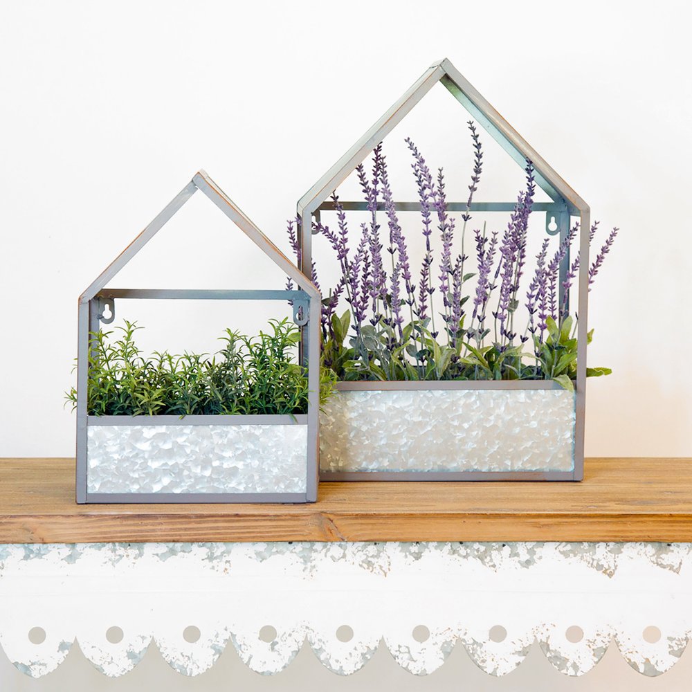 Two galvanized metal house-shaped hanging planters, one with green herbs and one with purple lavender, on a wooden shelf.