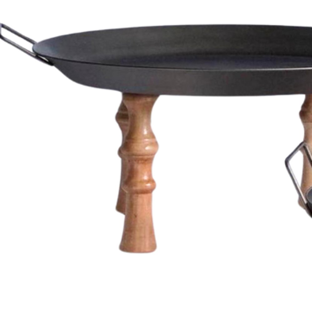 Round black metal tray with handles on carved brown wooden legs, isolated on white background.
